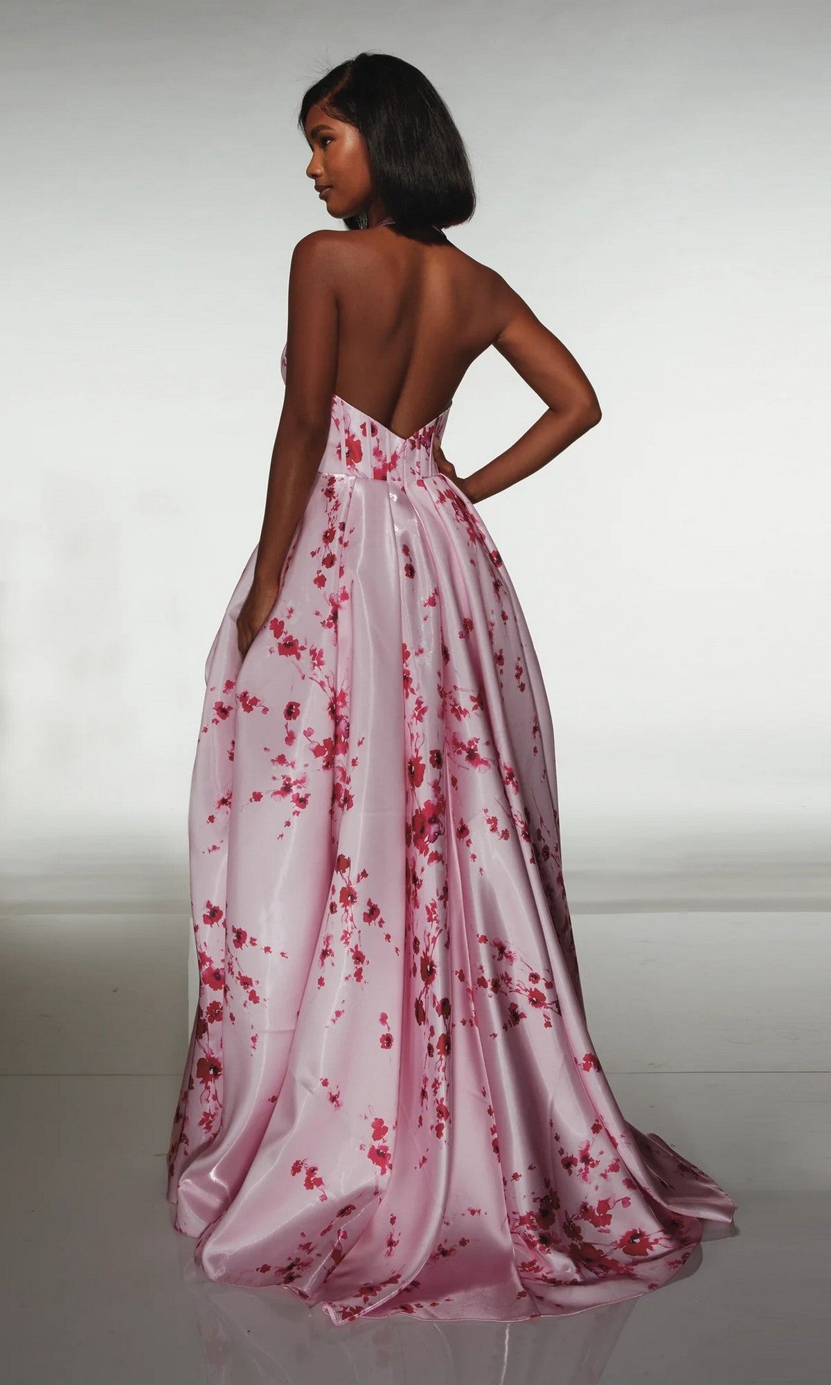 A woman stands with her back turned, wearing the strapless Long Formal Dress: Alyce 62214—a floor-length pink floral satin gown—against a neutral background.